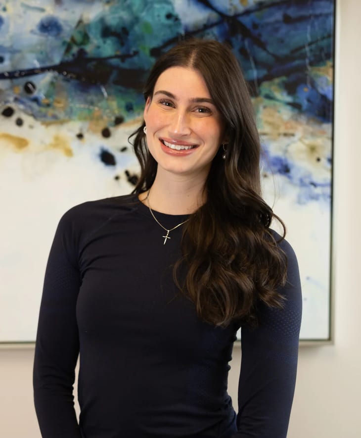 Nicole M. Evanovich, licensed aesthetician, smiling in front of an abstract blue painting