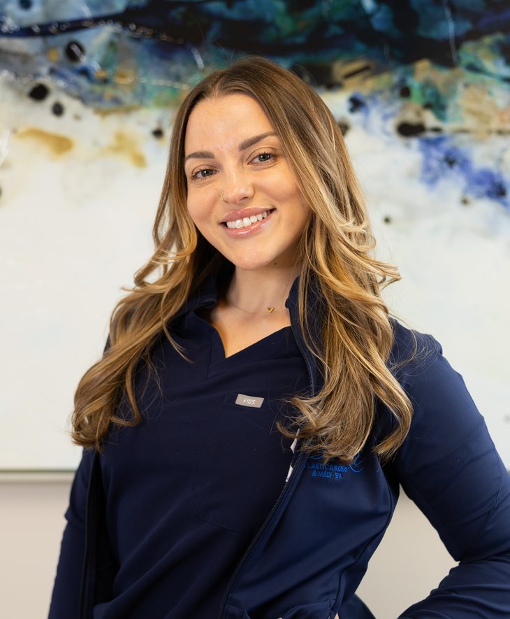 Allison D. Moore, licensed aesthetician, smiling in front of an abstract blue painting
