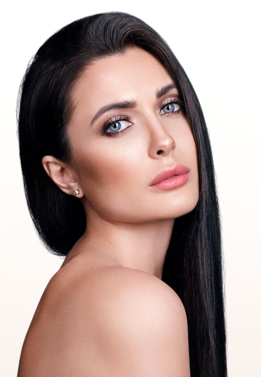 Woman with long black hair looking over a bare shoulder, with clear, even-toned skin